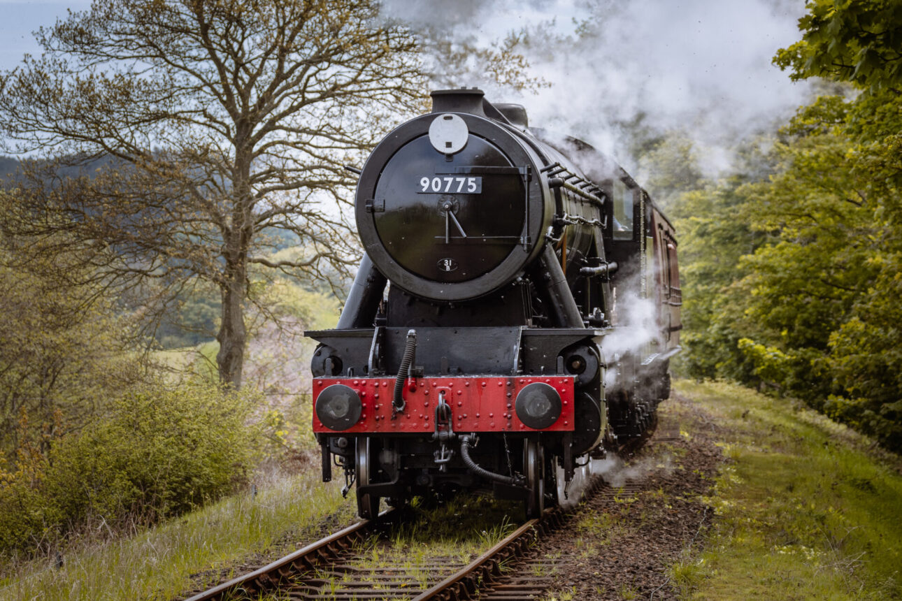 The Poppy Line classic steam train passing through forest trees